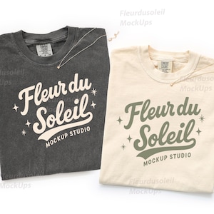 Könnte beinhalten: Zwei T-Shirts, eines in Anthrazitgrau und eines in Creme, werden gezeigt. Jedes Shirt trägt den Text "Fleur du Soleil MOCKUP STUDIO" in einer stilisierten Schriftart. Zarte goldene Halsketten mit Sternanhängern sind auf jedem Shirt drapiert.
