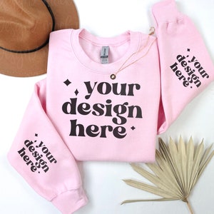 May include: Pink crewneck sweatshirt with the text "your design here" in black on the front and the same text on both sleeves.