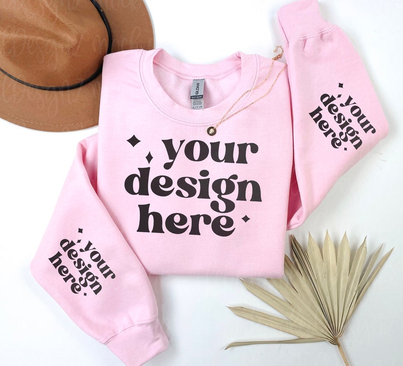 May include: Pink crewneck sweatshirt with the text "your design here" in black on the front and the same text on both sleeves.