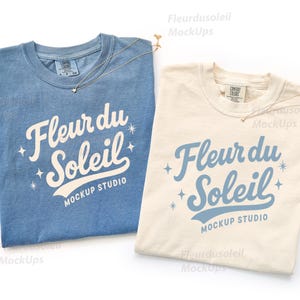May include: Two t-shirts, one blue and one cream, with the text "Fleur du Soleil" in a script font. Each shirt has a small star pendant necklace. The shirts are from Mockup Studio.