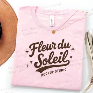 May include: A pale pink t-shirt featuring the text "Fleur du Soleil Mockup Studio" in brown. A gold necklace and a brown hat are on the left. Dried plants are on the right side of the shirt.