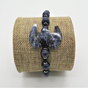 May include: A blue and white bat-shaped stone charm on a black cord bracelet with blue beads.
