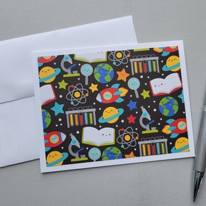 May include: A card with a black background and a colorful pattern of science-themed illustrations. The illustrations include planets, stars, rockets, microscopes, test tubes, and books. The card is perfect for a science-themed party or gift.