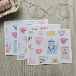 May include: Three white cards with a repeating pattern of teacups, teapots, and floral designs in pink, blue, and yellow.