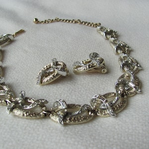 Könnte beinhalten: Ein Halsketten- und Ohrring-Set in Gold- und Silbertönen mit einem verlinkten Ketten-Design und klaren Strasssteinen.