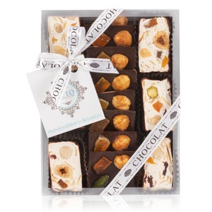 May include: A clear plastic box filled with assorted nougat and chocolate bars. The box is tied with a white ribbon with the words "Chocolat" printed on it. The box is labeled "& Co Chocolatier" and "Handcrafted in Brooklyn".