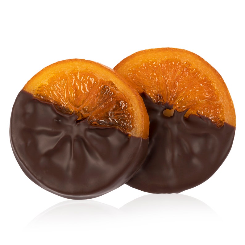 Op de afbeelding: Twee sinaasappelschijfjes gedoopt in donkere chocolade. De sinaasappelschijfjes zijn gekonfijt en hebben een glanzende afwerking. De chocolade is glad en bedekt de onderste helft van elk schijfje gelijkmatig.