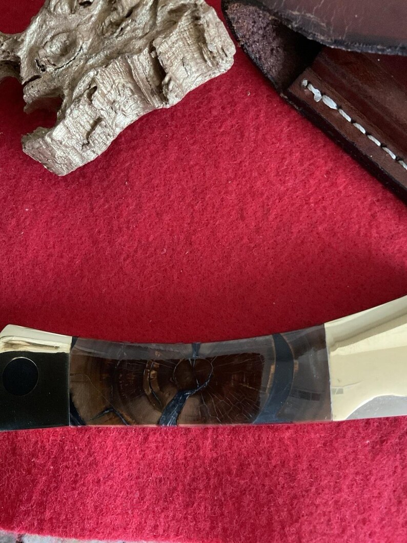 Puede incluir: Primer plano de una navaja de bolsillo con mango de madera y hoja plateada. El mango presenta un patr&oacute;n de vetas de madera oscura con detalles en negro y plata. La navaja est&aacute; parcialmente abierta, mostrando la hoja.