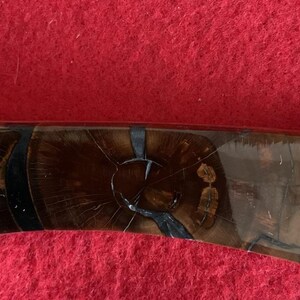 Puede incluir: Primer plano de un mango de cuchillo con un patr&oacute;n de vetas de madera marr&oacute;n oscuro. El mango est&aacute; acentuado con elementos negros y dorados. El cuchillo parece ser un art&iacute;culo hecho a mano, que muestra un dise&ntilde;o y una artesan&iacute;a &uacute;nicos.