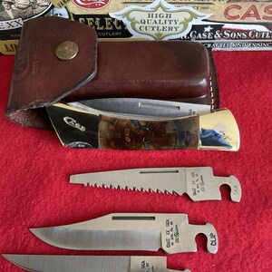 Puede incluir: Un estuche de cuero marr&oacute;n con un cierre dorado contiene una navaja plegable con un mango estampado. Se muestran tres hojas de acero inoxidable adicionales, cada una con un borde de corte diferente y el texto "CASE XX USA".