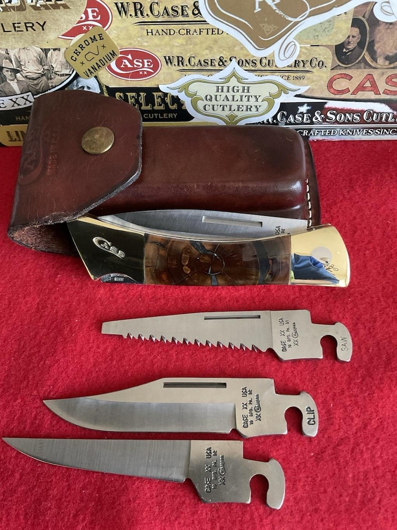 Puede incluir: Un estuche de cuero marr&oacute;n con un cierre dorado contiene una navaja plegable con un mango estampado. Se muestran tres hojas de acero inoxidable adicionales, cada una con un borde de corte diferente y el texto "CASE XX USA".