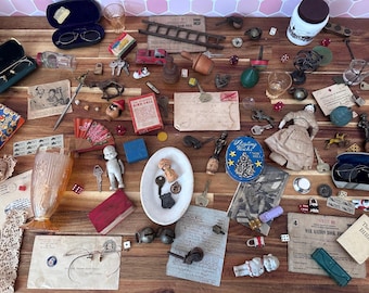 May include: A collection of vintage items, including eyeglasses, keys, dolls, dice, and miniature toys, arranged on a wooden surface. The items vary in color and size, creating a nostalgic and eclectic display. There are also small documents and a fan.