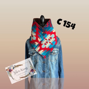 May include: A colorful neck warmer with a geometric pattern in red, turquoise, and cream colors. The neck warmer is fastened with gold-colored buttons and is displayed on a denim jacket. The text "C 154" is visible.