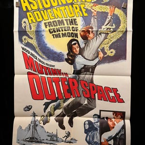 Op de afbeelding: Een vintage filmposter voor de film "Mutiny in Outer Space" met een stel in een dramatische omhelzing tegen een achtergrond van een draaiende melkweg. De poster is in de kleuren rood, wit en blauw met de titel in vetgedrukte rode letters.