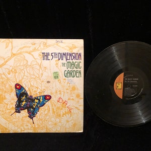 May include: A vintage vinyl record album cover featuring a colorful butterfly on a yellow background. The album is titled "The 5th Dimension - The Magic Garden".