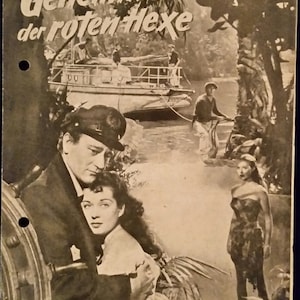 May include: A black and white movie poster for the film "Das Geheimnis der roten Hexe" featuring a couple embracing, a man in a boat, and a woman standing in the background.