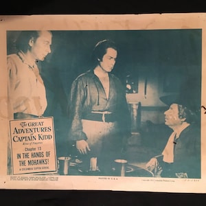 May include: A black and white photo of a scene from the movie serial "The Great Adventures of Captain Kidd". The text on the poster reads "Chapter 13 In the Hands of the Mohawks! A Columbia Super Serial".