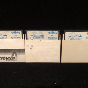 May include: Three black floppy disks labelled "The Black Cauldron" with the Walt Disney logo and "Sierra" logo. The disks are labelled "Disk 1", "Disk 2", and "Disk 3". The disks are in their original packaging with a Spinnaker logo.