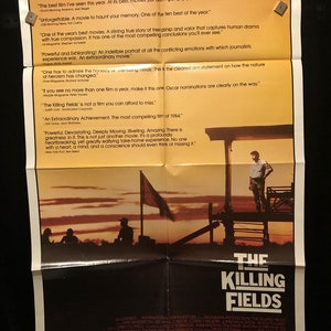 Puede incluir: Un cartel de película para "The Killing Fields" que muestra una escena de puesta de sol con tres hombres de pie en una plataforma de madera. El cartel incluye citas de varias publicaciones que elogian la película, incluyendo "¡Una película extraordinaria!" y "La película más convincente de 1984."