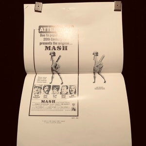 May include: A black and white poster advertising the movie "MASH" with the original cast. The poster features a peace sign with a military helmet on top. The text on the poster reads "Due to popular demand, 20th Century presents the original... MASH".