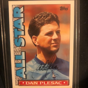 Puede incluir: Una tarjeta de béisbol con un jugador novato, Dan Plesac, con una camiseta azul y una firma blanca. La tarjeta es de la serie Topps All-Star.