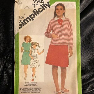 Può includere: Modello di cucito Simplicity numero 9985 per un vestito e un cardigan per bambina. Il modello mostra una bambina che indossa un cardigan a righe rosse e bianche con una gonna rossa e scarpe bianche. Il modello è disponibile nelle taglie 7, 8, 10, 12 e 14.