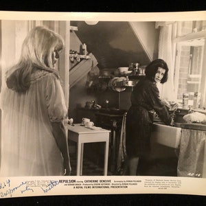 May include: Black and white photo of a scene from the movie Repulsion starring Catherine Deneuve. The photo is signed by the actress. The text on the photo reads "Repulsion starring Catherine Deneuve. Screenplay by Roman Polanski and Gerard Brach. Produced by  Eustache  Goutwiller. Directed by Roman Polanski. A Royal Films International Presentation."