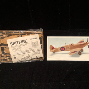 May include: A plastic model kit of a Spitfire airplane with a brown and tan color scheme. The kit includes instructions and a picture of a finished model with the text "RODB" on the side.