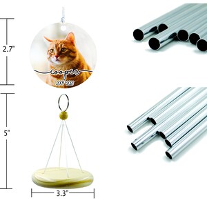 May include: A personalized wind chime featuring a round pendant with a cat portrait and the name "cooper" with dates 2009-2021. The wind chime is 5 inches tall with a 3.3-inch wooden base. Includes silver-colored metal tubes.