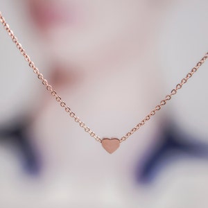 K&ouml;nnte beinhalten: Halskette aus Ros&eacute;gold mit einem kleinen Herzanh&auml;nger. Die Kette ist ein feines Kettendesign, und das Herz hat eine glatte, solide Form. Die Halskette wird vor einem weichen, verschwommenen Hintergrund pr&auml;sentiert, der die schlichte Eleganz des Schmucks hervorhebt.