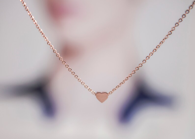 K&ouml;nnte beinhalten: Halskette aus Ros&eacute;gold mit einem kleinen Herzanh&auml;nger. Die Kette ist ein feines Kettendesign, und das Herz hat eine glatte, solide Form. Die Halskette wird vor einem weichen, verschwommenen Hintergrund pr&auml;sentiert, der die schlichte Eleganz des Schmucks hervorhebt.