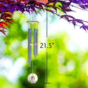 May include: A 21.5-inch wind chime with silver-colored tubes and a wooden top and bottom. A round, wooden pendant at the bottom features a dog portrait and the name "Lola". The chime hangs from a tree branch with purple leaves.