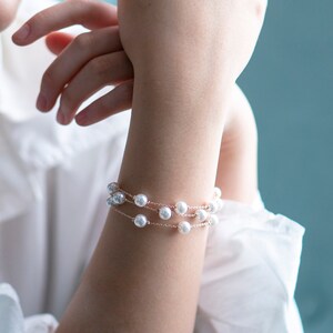 May include: A delicate bracelet featuring three strands of faux pearls. The bracelet is made of a thin, gold-colored chain. The pearls are white and round. The bracelet is worn on the wrist.