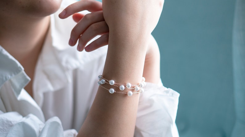 May include: A delicate bracelet featuring three strands of faux pearls. The bracelet is made of a thin, gold-colored chain. The pearls are white and round. The bracelet is worn on the wrist.