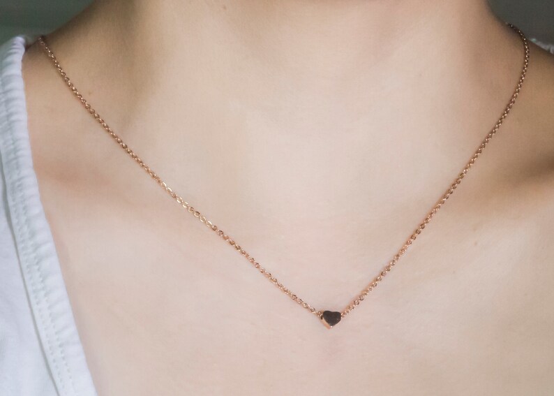 K&ouml;nnte beinhalten: Eine zarte Halskette aus Ros&eacute;gold mit einem kleinen Herzanh&auml;nger. Die Kette ist fein und das Herz hat einen dunkleren Ros&eacute;goldton. Die Halskette wird vor einem neutralen Hintergrund pr&auml;sentiert.