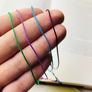 Peut inclure: Cinq cordons de diff&eacute;rentes couleurs, vert, violet, bleu et deux nuances de violet, sont tenus dans une main. Les cordons sont tous li&eacute;s ensemble &agrave; l'extr&eacute;mit&eacute;.