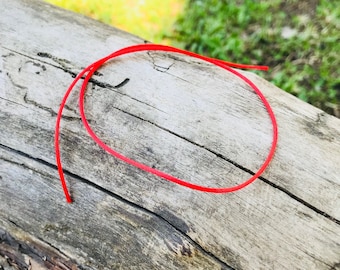 Könnte beinhalten: Eine rote Schnur ist auf einem Stück verwittertem Holz gewickelt.