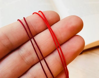 May include: Two spools of red string, one a darker burgundy red and the other a brighter red, are held in a hand.