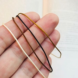 May include: Four spools of cord in different colours: white, brown, dark brown, and gold.