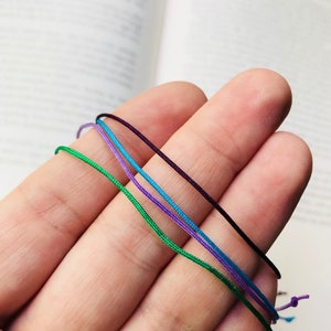 Peut inclure: Quatre brins de cordon de diff&eacute;rentes couleurs&nbsp;: vert, bleu, violet et noir. Les cordons sont tenus dans une main.