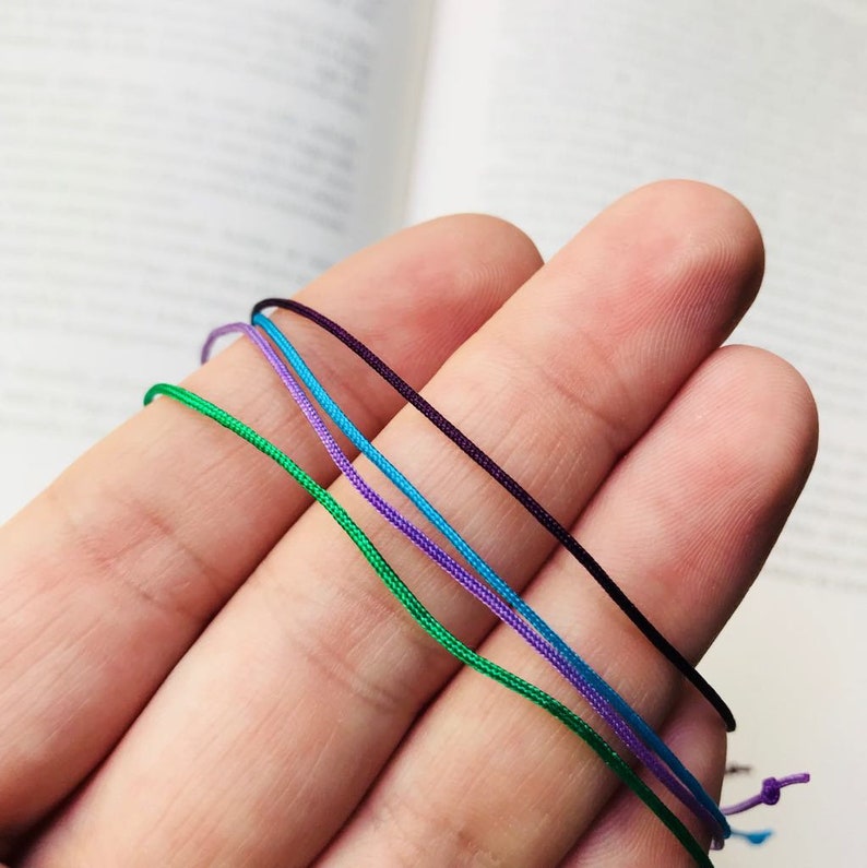 Peut inclure: Quatre brins de cordon de diff&eacute;rentes couleurs&nbsp;: vert, bleu, violet et noir. Les cordons sont tenus dans une main.