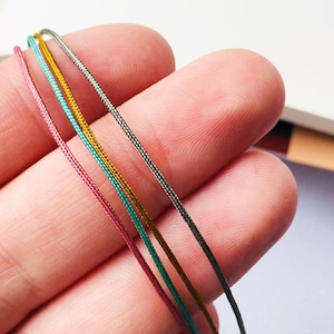 May include: Four spools of waxed cord in different colors: pink, teal, gold, and silver.