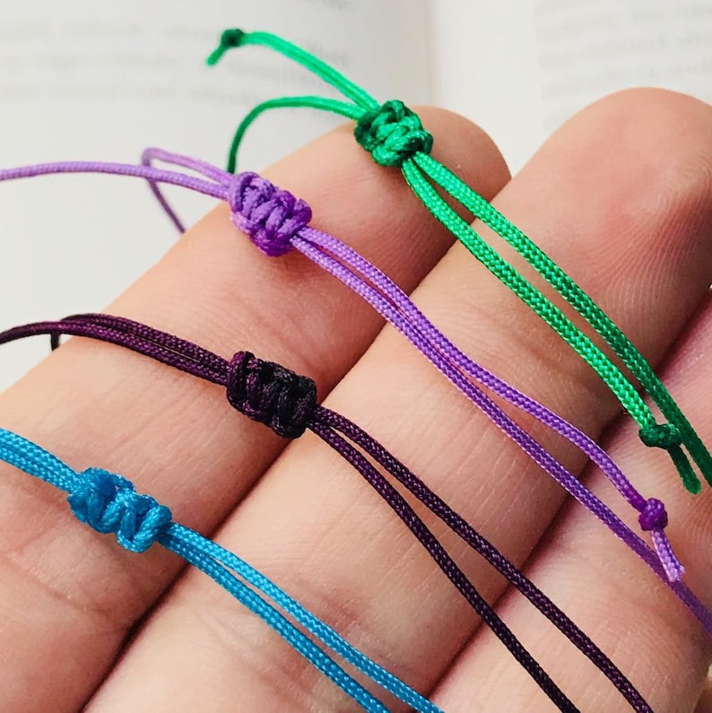 Peut inclure: Quatre bracelets color&eacute;s avec des extr&eacute;mit&eacute;s nou&eacute;es. Les bracelets sont turquoise, violet, violet fonc&eacute; et vert.