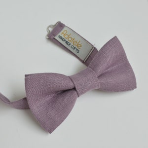 May include: A mauve linen bow tie with an adjustable strap. The strap has a white label with the text "Adatele Handmade Gifts".
