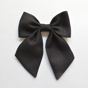 Könnte beinhalten: Eine schwarze Fliege aus Leinen, ein klassisches Accessoire. Die Fliege besteht aus strukturiertem Stoff und hat lange, spitz zulaufende Enden. Ein stilvolles Accessoire für formelle oder lässige Kleidung.