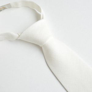 May include: A white linen tie with an adjustable strap. The tie is made of a soft, lightweight fabric and has a subtle sheen. The strap is made of a durable material and has a secure closure.