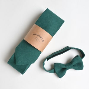 May include: A dark green linen necktie and matching bow tie. The necktie has a brown label with the text "ADATÉLÉ" on it.