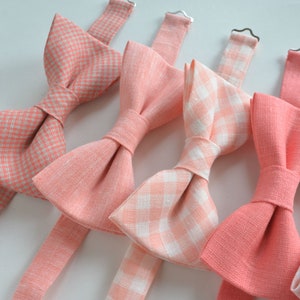 May include: Five bow ties in various shades of pink and white. Some are solid pink, while others have a white gingham pattern.