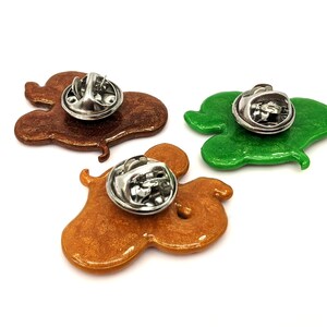 The backs of three snake pins with stainless steel clasps - one golden brown, one brown and one green, all with sparkle.
