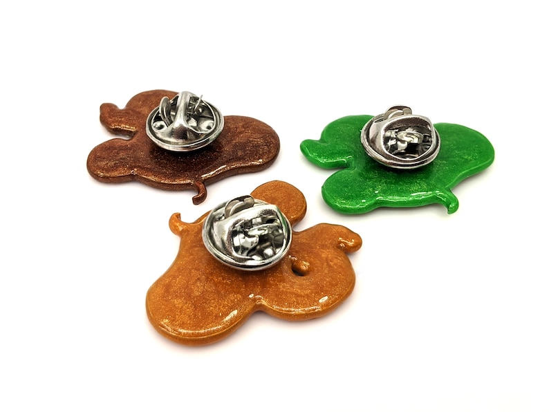 The backs of three snake pins with stainless steel clasps - one golden brown, one brown and one green, all with sparkle.